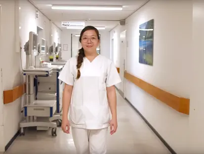 A person in white professional clothing walks through a hospital corridor.