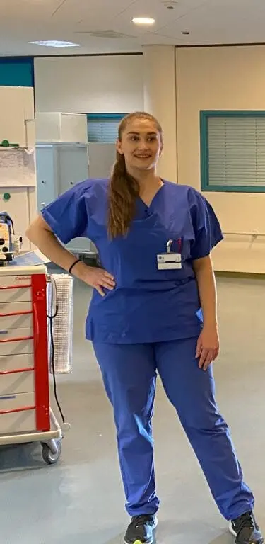 Woman in blue medical clothing posing for a camera in a hospital.