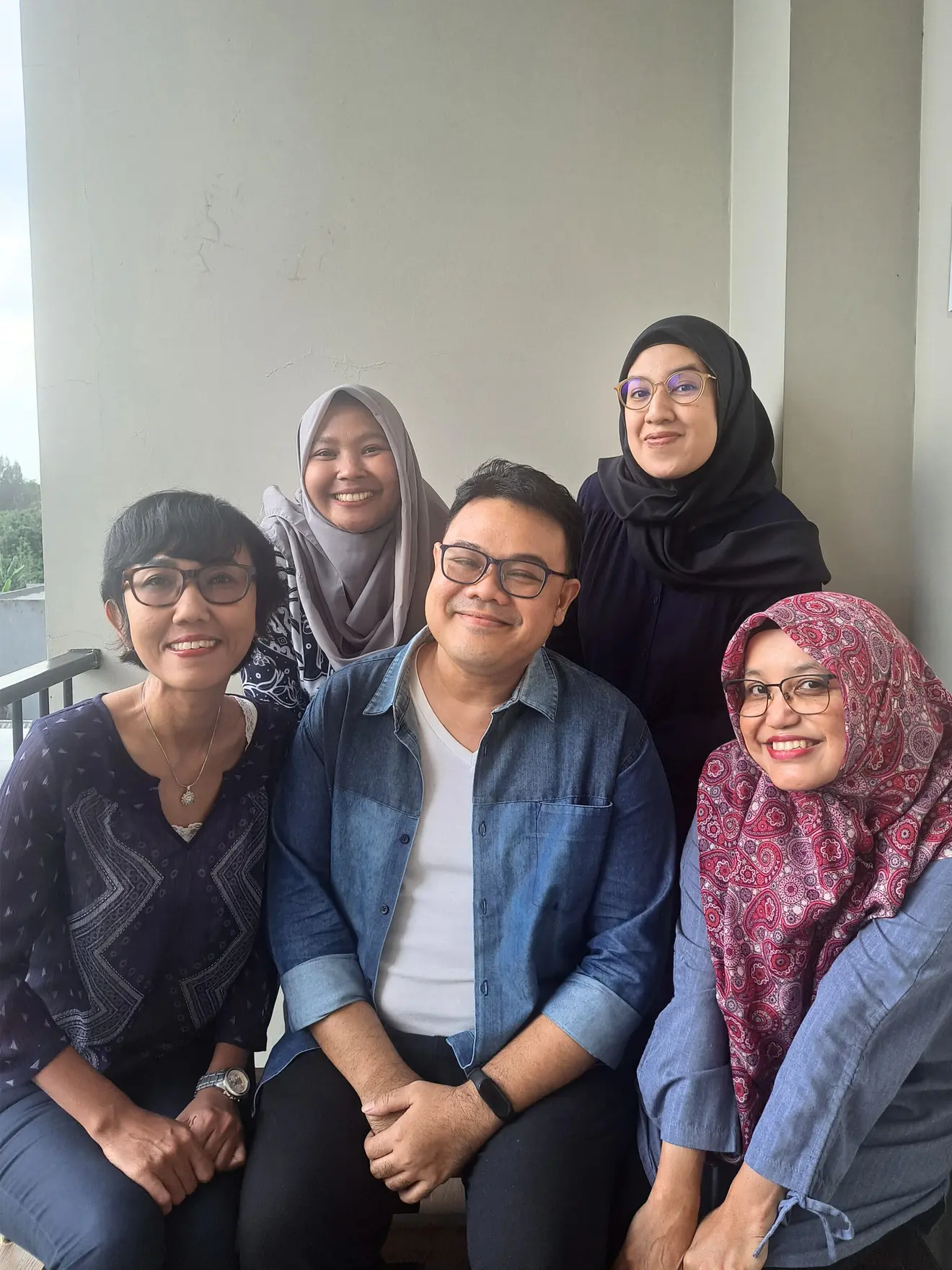 Five people pose smiling in front of a wall, two are sitting and three are standing behind them.